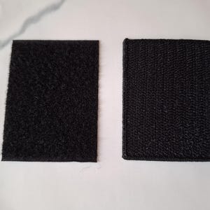 May include: Two black hook and loop fastener squares. One has a fuzzy texture, and the other has a woven texture. Both are rectangular and lie on a white surface. These are commonly used for securing items.