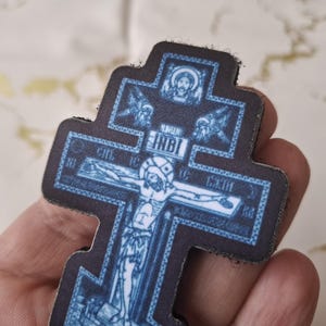 Pu&ograve; includere: Una croce ortodossa blu e nera con una raffigurazione di Ges&ugrave; Cristo. La croce presenta dettagli intricati e testo religioso. La croce &egrave; tenuta in una mano.
