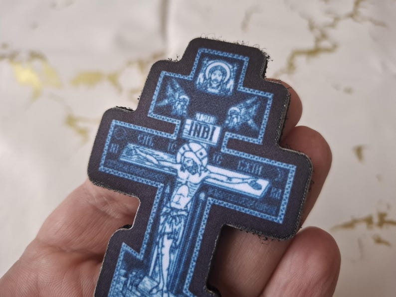 Pu&ograve; includere: Una croce ortodossa blu e nera con una raffigurazione di Ges&ugrave; Cristo. La croce presenta dettagli intricati e testo religioso. La croce &egrave; tenuta in una mano.