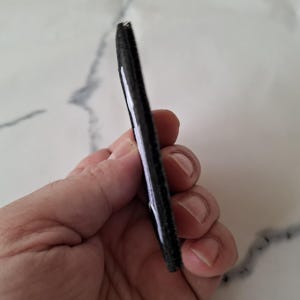 May include: A black, rectangular object with a white stripe along one edge. The object appears to be made of a textured material. The item is held in a hand.
