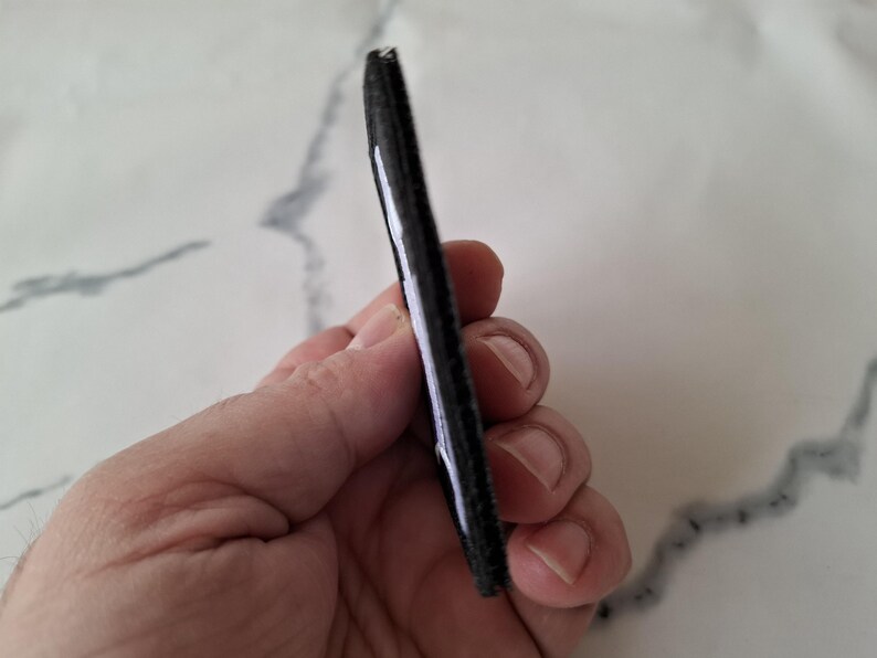 May include: A black, rectangular object with a white stripe along one edge. The object appears to be made of a textured material. The item is held in a hand.