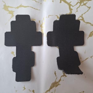 Pu&ograve; includere: Due cuscinetti in schiuma neri a forma di croce con superfici strutturate. Un cuscinetto ha un bordo netto, mentre l'altro ha un bordo sfilacciato. I cuscinetti sono esposti su una superficie bianca con marmorizzazione dorata.