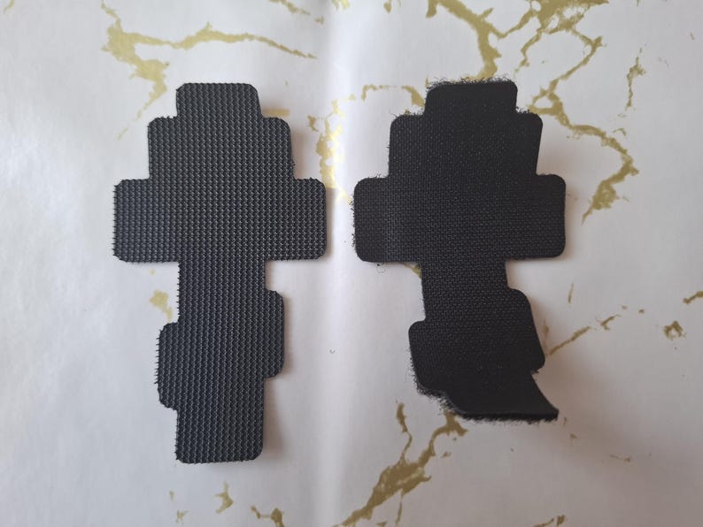 Pu&ograve; includere: Due cuscinetti in schiuma neri a forma di croce con superfici strutturate. Un cuscinetto ha un bordo netto, mentre l'altro ha un bordo sfilacciato. I cuscinetti sono esposti su una superficie bianca con marmorizzazione dorata.