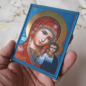 K&ouml;nnte beinhalten: Ein religi&ouml;ser Icon-Patch mit einer Darstellung der Jungfrau Maria und des Kindes. Das Bild hat einen goldenen Heiligenschein und wird von einem blauen Rand umrahmt. Die Jungfrau Maria tr&auml;gt eine rote Kopfbedeckung und ein rotes Gewand.