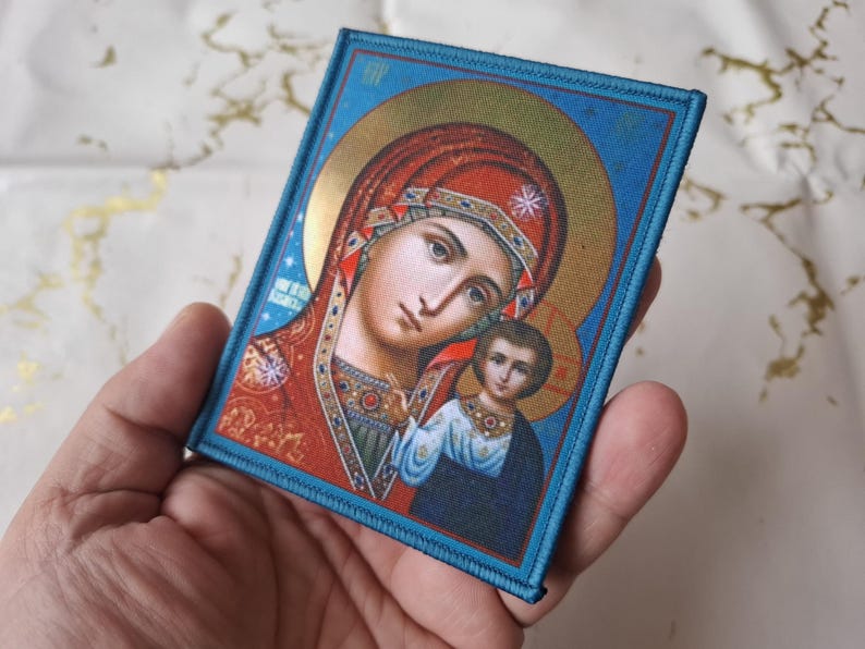 K&ouml;nnte beinhalten: Ein religi&ouml;ser Icon-Patch mit einer Darstellung der Jungfrau Maria und des Kindes. Das Bild hat einen goldenen Heiligenschein und wird von einem blauen Rand umrahmt. Die Jungfrau Maria tr&auml;gt eine rote Kopfbedeckung und ein rotes Gewand.