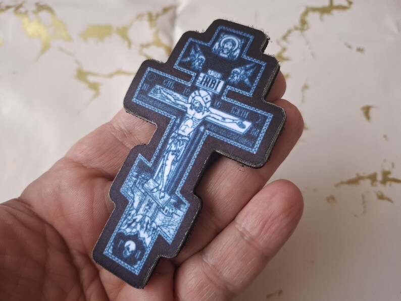 Pu&ograve; includere: Croce ortodossa blu e nera con una raffigurazione di Ges&ugrave; Cristo. La croce presenta dettagli intricati e testo, con un bordo scuro. &Egrave; un oggetto religioso.