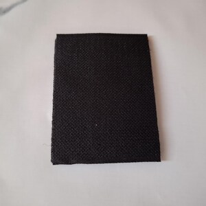 May include: A rectangular piece of black fabric with a textured weave, set against a white background. The fabric's edges are neatly cut, presenting a simple, clean appearance. The material appears to be sturdy.