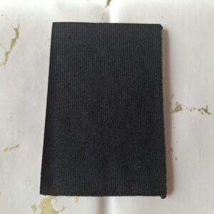 May include: A rectangular piece of black fabric with a textured, ribbed surface. The fabric is displayed against a white background with gold-colored accents. The fabric appears to be a sample or swatch.