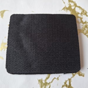 May include: A black rectangular patch of fabric with a textured surface.