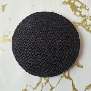 Op de afbeelding: Een ronde, zwarte, stoffen patch met een textuur.