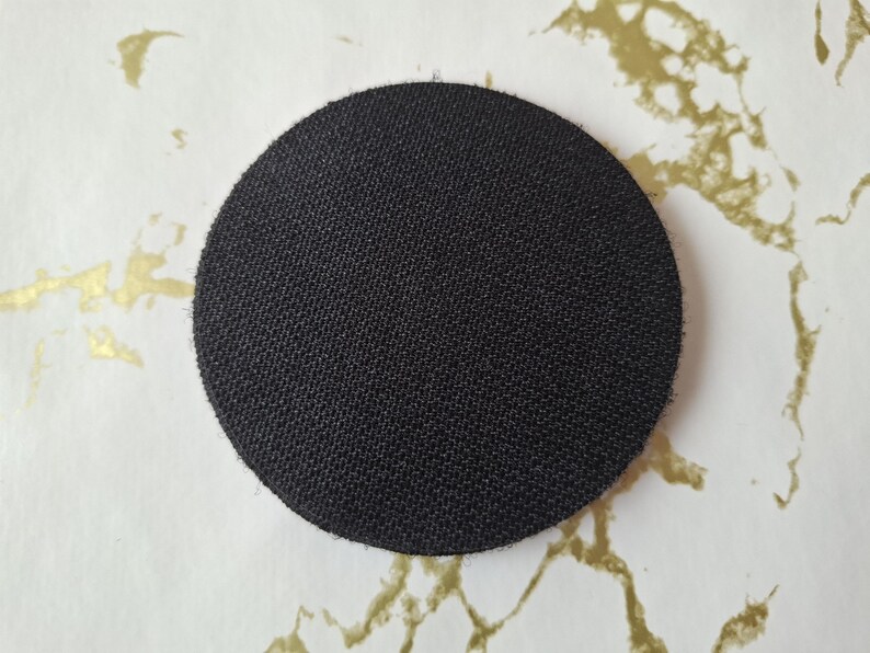 Op de afbeelding: Een ronde, zwarte, stoffen patch met een textuur.