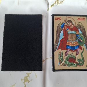 May include: A rectangular black hook and loop patch next to a rectangular patch with an illustration of a figure in armor slaying a dragon. The illustration has the text "APX" and "MHX".