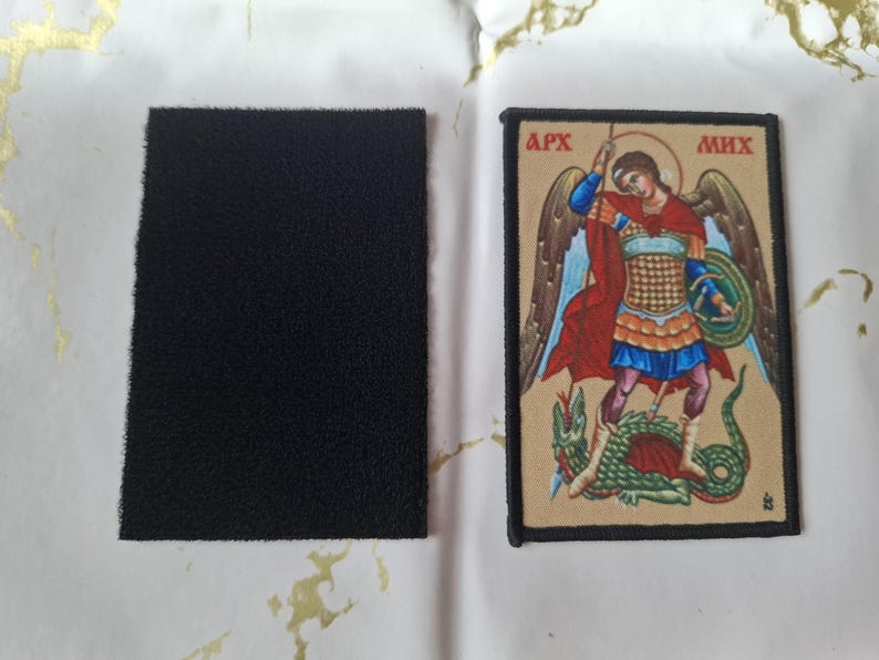 May include: A rectangular black hook and loop patch next to a rectangular patch with an illustration of a figure in armor slaying a dragon. The illustration has the text "APX" and "MHX".