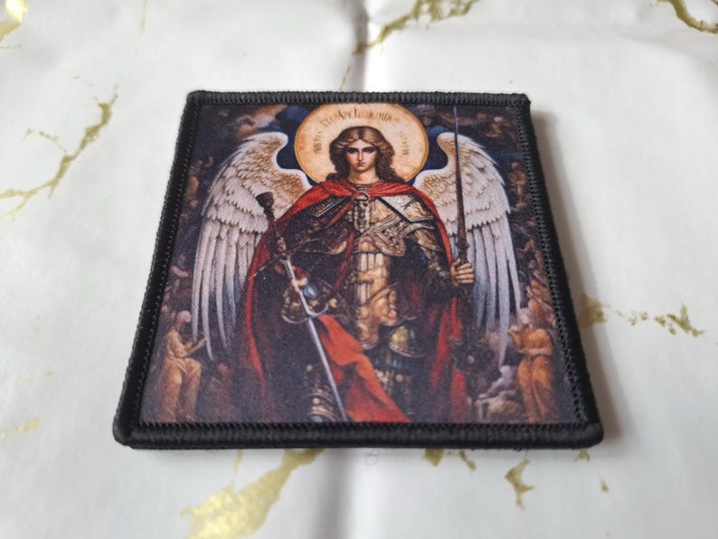 May include: Square patch featuring a detailed illustration of an angel with large white wings, a red cloak, and a sword. The angel has a halo and is set against a dark background. The patch has a black border.