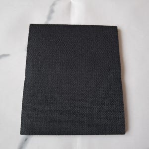 Op de afbeelding: Een vierkante, zwarte stoffen patch met een getextureerd oppervlak. De patch is gemaakt van een strak geweven materiaal en is geplaatst tegen een witte achtergrond.