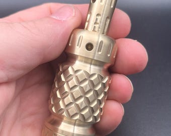 May include: A cylindrical brass object with a metallic gold finish, featuring a textured diamond-patterned centre section, a smooth neck with small circular holes, and grooved detailing on the top and bottom ends of the metal component.
