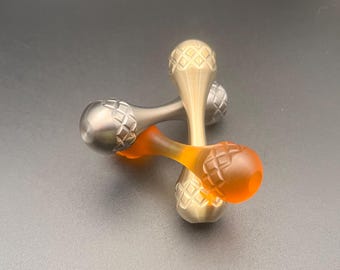 May include: Two dumbbell-shaped objects with rounded ends featuring a textured diamond-patterned grid. One object is a metallic gold colour, and the other is a translucent orange material. Both items have a smooth, narrow centre section.