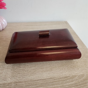 Peut inclure: Une boîte en bois rouge foncé avec un couvercle à charnières et un petit bouton sur le dessus.