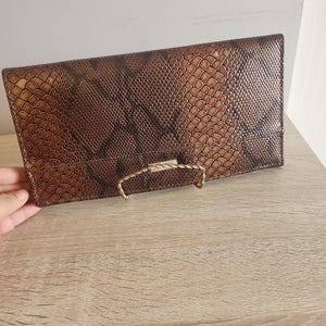May include: A brown snakeskin-patterned clutch purse with a gold clasp.