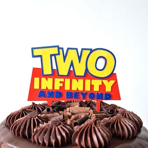 May include: A chocolate cake with chocolate frosting and decorative chocolate swirls. The cake is topped with a red sign that reads "TWO INFINITY AND BEYOND" in yellow and blue lettering. A celebratory dessert for a birthday.