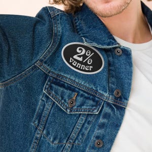 May include: A black and white oval patch with the text "2% vanner" on a blue denim jacket.