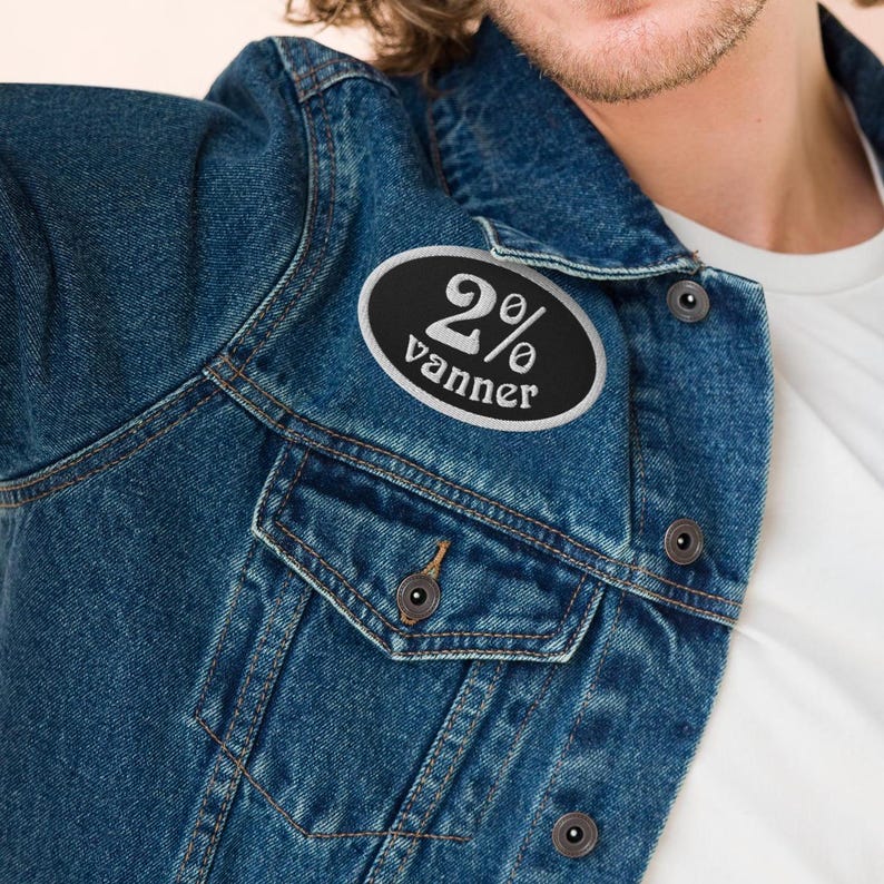 May include: A black and white oval patch with the text "2% vanner" on a blue denim jacket.