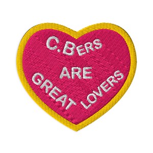Può includere: Un cerotto a forma di cuore rosa con un bordo giallo. Il cerotto ha un testo bianco che dice "C.BERS ARE GREAT LOVERS".