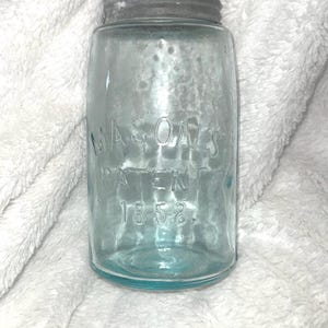 Peut inclure: Un bocal Mason's Patent 1858 teinté de bleu vintage avec un couvercle en métal. Le bocal porte l'inscription en relief "MASON'S PATENT 1858". Le bocal en verre est cylindrique.