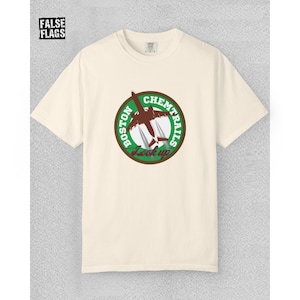 Könnte beinhalten: Cremefarbenes T-Shirt mit einem kreisförmigen Aufdruck mit der Aufschrift "Boston Chemtrails Look Up". Die Grafik zeigt ein braunes Flugzeug und grüne und weiße Akzente. Der Text "FALSE FLAGS" befindet sich in der oberen linken Ecke.