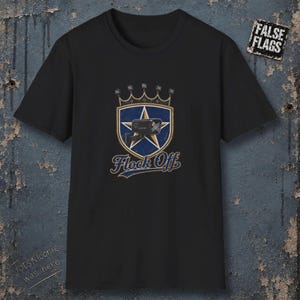 Könnte beinhalten: Ein schwarzes Kurzarm-T-Shirt mit einer Grafik, die einen blauen Schild mit einem goldenen Stern und einer Überwachungskamera zeigt. Über dem Schild befindet sich eine Krone, darunter steht der Text "Flock Off". Oben rechts ist ein "FALSE FLAGS"-Etikett zu sehen.