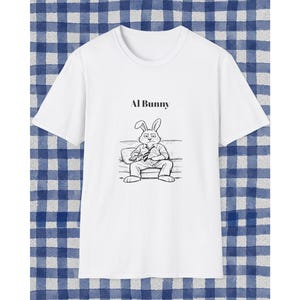 Puede incluir: Camiseta blanca con una ilustración de dibujos animados en blanco y negro de un conejo con corbata sentado en un sofá. El texto "Al Bunny" está encima de la ilustración.