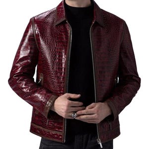 Puede incluir: Chaqueta de cuero burdeos con textura de piel de cocodrilo. La chaqueta tiene cierre de cremallera, cuello y ribetes marrones. La persona lleva un cuello alto negro debajo. Prenda de vestir exterior elegante.