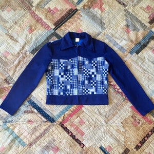 May include: A vintage blue jacket with a patchwork design on the front. The jacket has long sleeves, a collar, and a full zipper. The patchwork features various shades of blue and white squares.