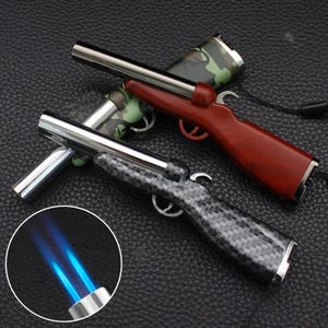 May include: Three novelty lighters shaped like rifles. One has a dark wood finish, another a carbon fiber pattern, and the third a camouflage design. Each has a silver barrel and trigger.