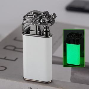 May include: A white lighter with a black dragon head on top. The lighter glows green in the dark.
