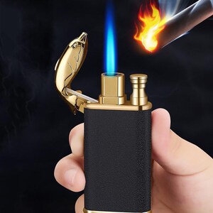 May include: A black and gold lighter with a dolphin-shaped lid. The lighter is lit and has a blue flame.
