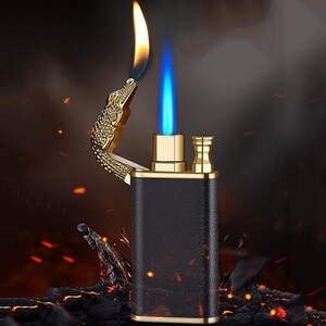May include: A black and gold lighter with a crocodile design. The lighter has a blue flame and is lit.