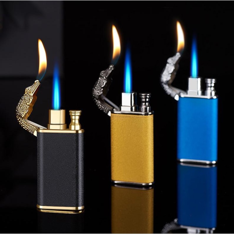 May include: Three butane lighters with alligator head designs. The lighters are black, gold, and blue. Each lighter has a double flame.