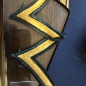 May include: Two gold and black chevron patches sewn together. The chevrons are embroidered with gold thread on a black fabric background.