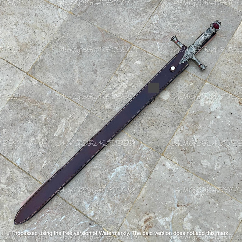 May include: A decorative sword with a silver hilt and a burgundy leather sheath. The sword features intricate detailing on the hilt and a red gem at the pommel. The sheath is a deep burgundy color, and the sword is laid out on a stone surface.
