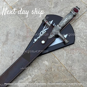 May include: An ornate silver dagger with red accents and a decorative handle, resting in a brown leather sheath. The sheath is placed on a black surface with a white design. The text "Next day ship" is visible.