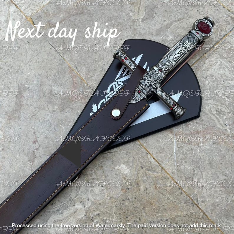 May include: An ornate silver dagger with red accents and a decorative handle, resting in a brown leather sheath. The sheath is placed on a black surface with a white design. The text "Next day ship" is visible.