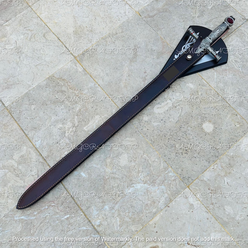 May include: A decorative sword with a silver handle and a red gem at the top. The sword is in a brown leather sheath. The sheath is attached to a black display stand. The sword is approximately 30 inches long.