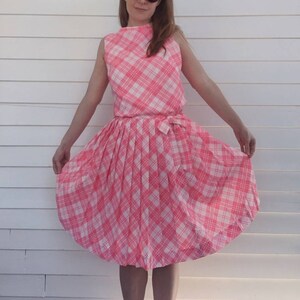 Könnte beinhalten: Ein rosa-weiß kariertes Kleid mit einem Faltenrock. Das Kleid hat einen ärmellosen Oberteil und eine Schleife an der Taille.
