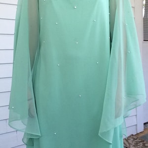 K&ouml;nnte beinhalten: Ein mintgr&uuml;nes Maxikleid mit durchsichtigen, flie&szlig;enden &Auml;rmeln und einem Perlenbesatz am Ausschnitt.