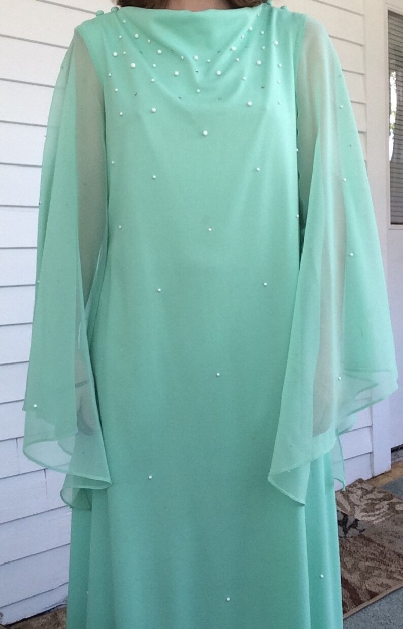 K&ouml;nnte beinhalten: Ein mintgr&uuml;nes Maxikleid mit durchsichtigen, flie&szlig;enden &Auml;rmeln und einem Perlenbesatz am Ausschnitt.