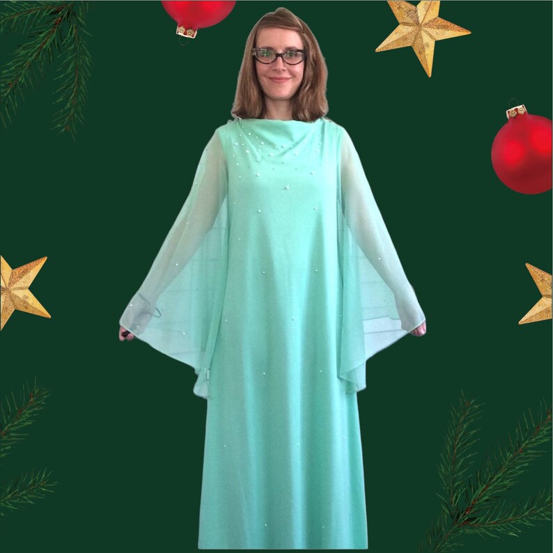 K&ouml;nnte beinhalten: Eine Frau tr&auml;gt ein mintgr&uuml;nes, lang&auml;rmeliges Kleid mit einem Perlenbesatz am Ausschnitt. Das Kleid hat einen flie&szlig;enden, kapenartigen Schnitt und ist perfekt f&uuml;r einen formellen Anlass.