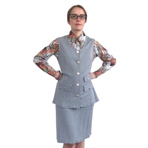 May include: A light blue skirt suit with a vest and a skirt. The vest has a V-neck and buttons down the front. The skirt is knee-length and has pockets on the sides.
