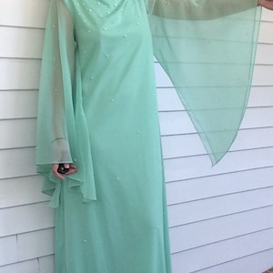 K&ouml;nnte beinhalten: Ein langes, mintgr&uuml;nes Maxikleid mit durchsichtigen Glocken&auml;rmeln und einem perlenbesetzten Oberteil.