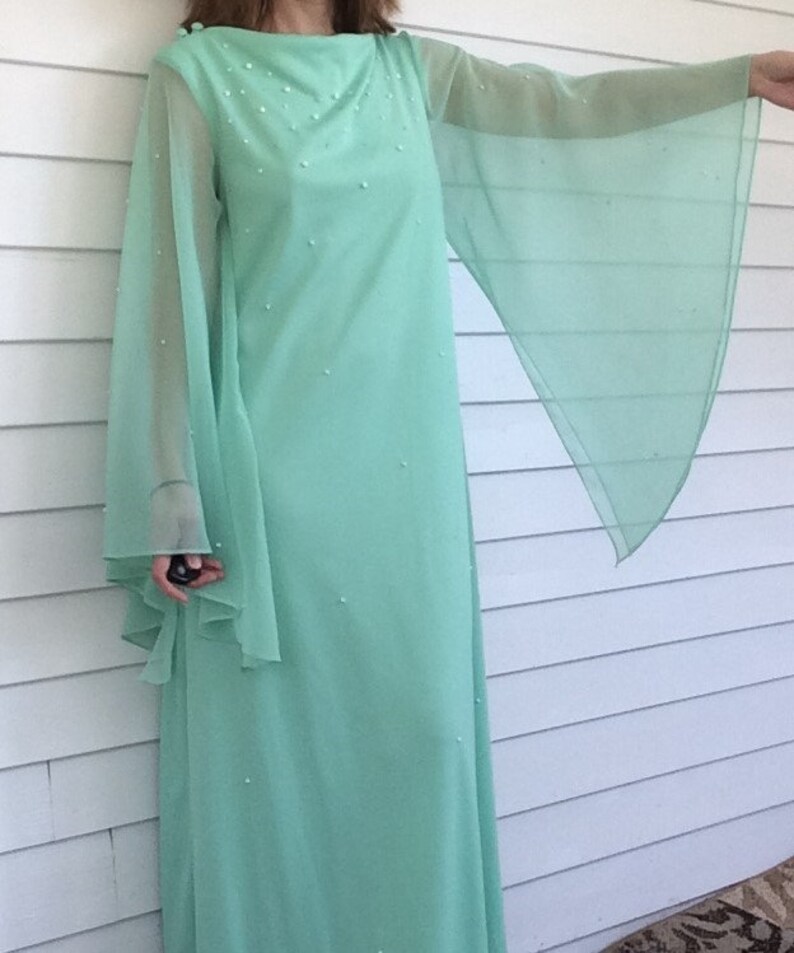 K&ouml;nnte beinhalten: Ein langes, mintgr&uuml;nes Maxikleid mit durchsichtigen Glocken&auml;rmeln und einem perlenbesetzten Oberteil.